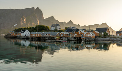 22 july 2025, Reine, Norway. Sakrisøy island, on Lofoten islands, typical wooden ochre colored buildings, mountains in background. Early morning sunlight. Wonderful travel destination, northern Europe © Dirk