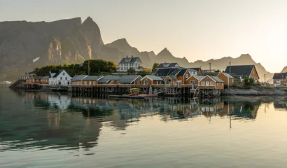 Fototapete Lofoten 22 july 2025, Reine, Norway. Sakrisøy island, on Lofoten islands, typical wooden ochre colored buildings, mountains in background. Early morning sunlight. Wonderful travel destination, northern Europe  © Dirk