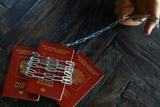 Russian Passports Restrained by Handcuffs and Paper Clips on Dark Wood Surface
