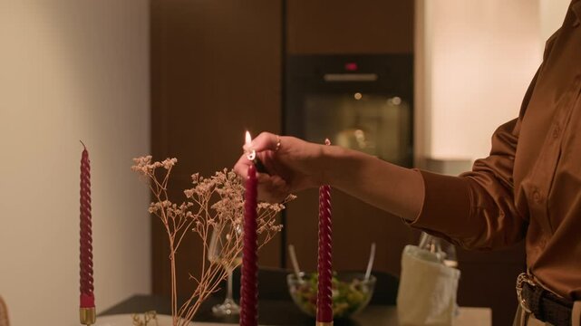 Handheld shot of young Caucasian woman lighting candles on table while preparing for romantic home dinner with boyfriend