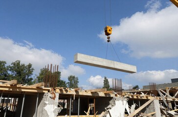 Naklejka premium Construction Site with Crane Lifting Concrete Beam for Building Framework Under Blue Sky