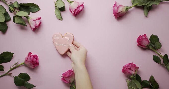 Woman hand placing Be My Valentine heart cookie inside pink rose frame