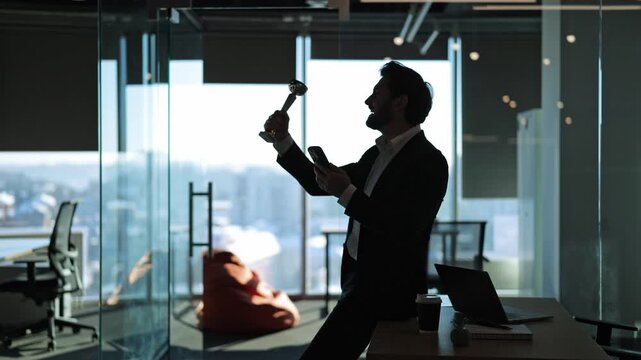 Professional expresses joy and triumph, celebrating a significant business achievement. Holding a trophy and smartphone, symbolizing success in a modern office environment.
