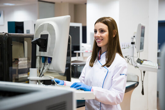 Young woman in white apparel using sample analyzer while working in research lab