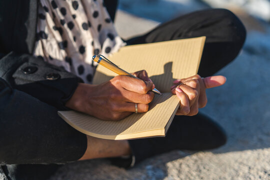 Woman sitting on a wall writing in notebook, close-up