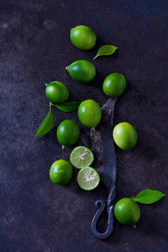 Sliced and whole limequats, leaves and old knife on dark ground