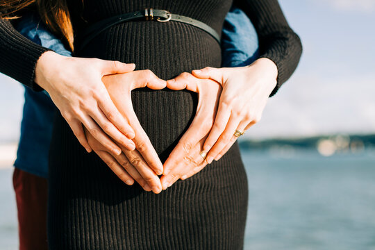 Affectionate expectant parents shaping a heart with their hands on baby belly