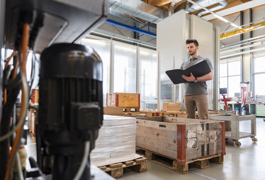 Man with folder standing in factory storeroom