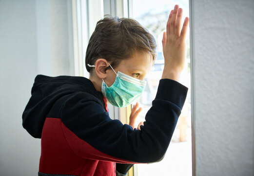 Sad boy with mask looking out of window