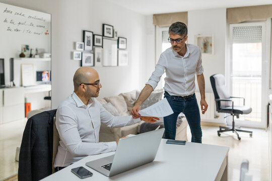 Two colleagues working at home with laptop and documents