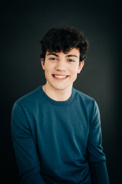Smiling young man in blue shirt against dark studio background