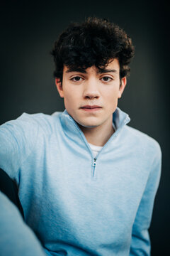Serious young man in light blue pullover against dark backdrop
