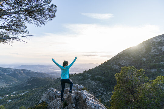 Woman celebrating reaching mountain summit at sunrise