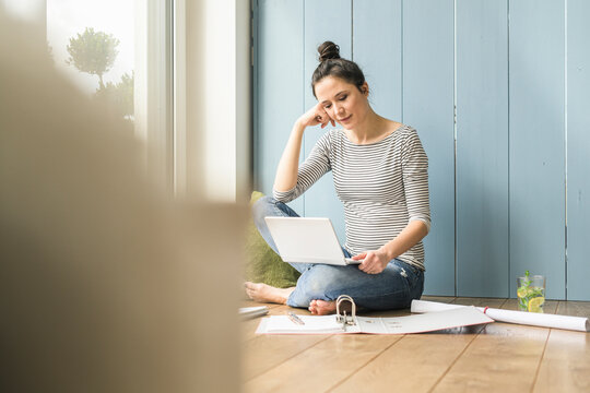 Woman sitting at the window at home working with laptop and file folder