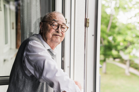 Portrait of smiling senior man standing at open window