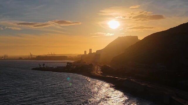 Alicante al atardecer desde el mar con el sol detr&aacute;s del Castillo de Santa Barbara , panor&aacute;mica a&eacute;rea