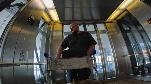 Travel POV: Man with luggage cart enters glass elevator in CPT airport