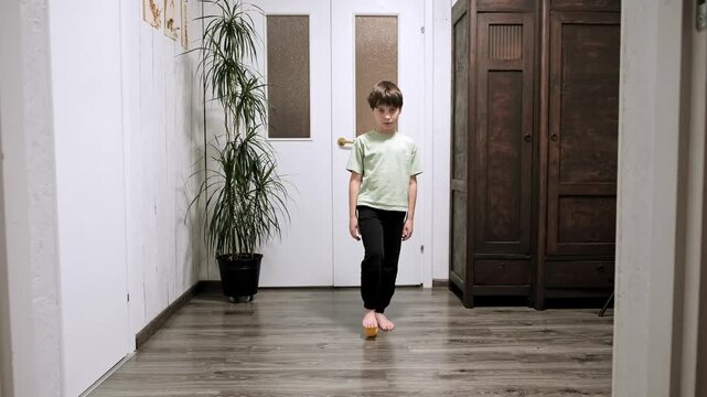 Barefeet boy massaging the foot with spiky massage ball applying pressure to feet soles surface. The prickly yellow ball, treatment of flat feet. Child performs physical therapy exercises. 4k footage.