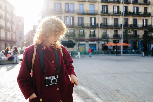 Young woman with camera searching through pockets on city street