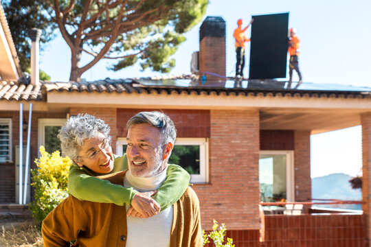 Playful couple outdoors during solar panel installation at home