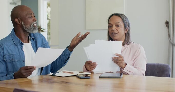 Couple, African American man showing sheet and woman scanning stack at wooden table, sorting bills