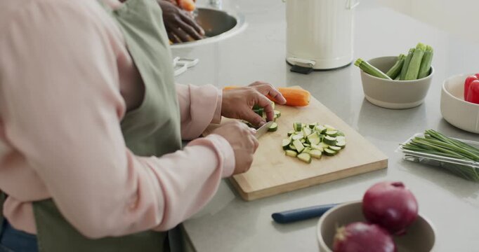 Counter cook is starting to slice zucchini as sink-helper is rinsing carrot, prepping veg for meal