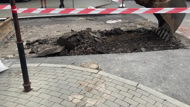 Excavators bucket is actively lifting and removing broken pieces of asphalt during urban road maintenance work. Trench in construction site, close up heavy machinery backhoe digger. City renivation