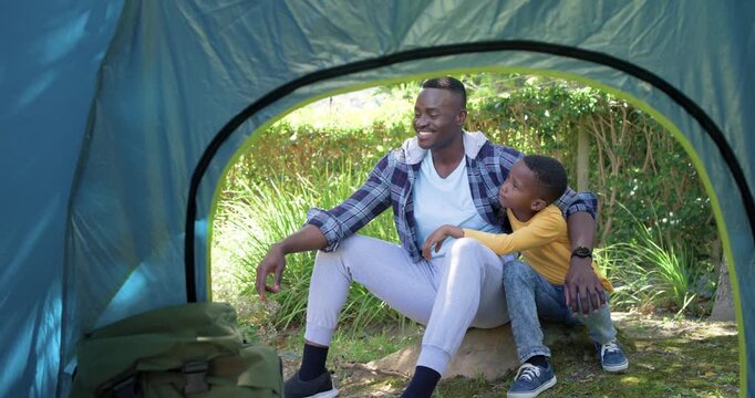 Dad and son are sitting by blue tent, dad is spotting, pointing skyward to show him