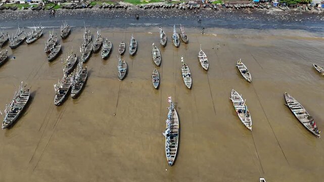 top-down drone perspective showing dozens of traditional wooden fishing pirogues arranged on the black volcanic sand of Limbe beach Cameroon