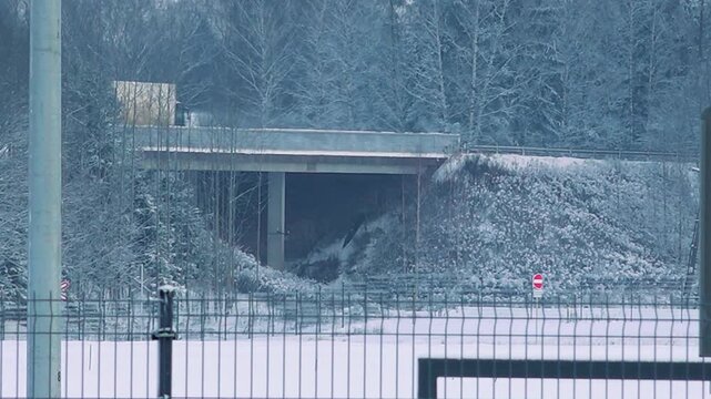 A truck drives over a snowy overpass surrounded by frost-covered trees