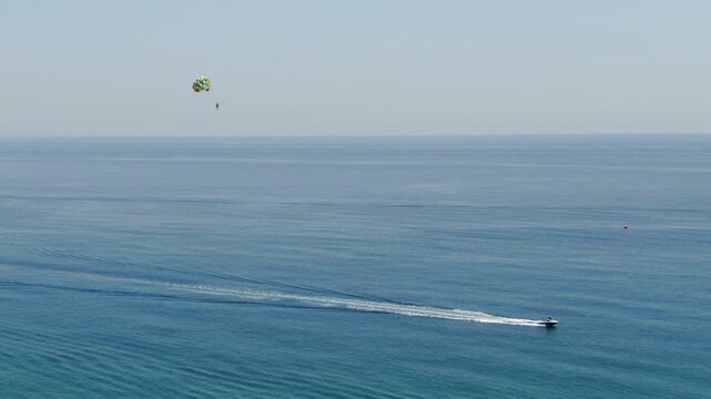 Minimalist aerial view of speed boat towing a parasailer high above the calm deep blue Ionian Sea on a sunny summer day in Greece