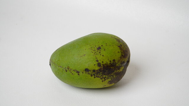 An Arumanis mango (Mangifera indica) with green skin and black spots on it is placed in a white place (isolated white).
