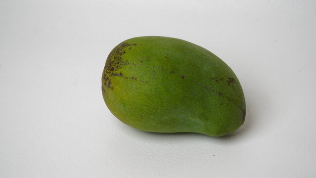 An Arumanis mango (Mangifera indica) with green skin and black spots on it is placed in a white place (isolated white).