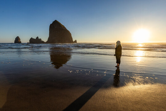 USA, Oregon, Cannon Beach, Woman standing on beach near haystack rock at sunset