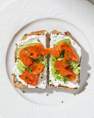 Toast with smoked salmon sliced avocado and cream cheese topped with fresh chives on white plate