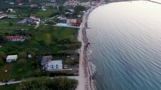 Aerial drone flight along the long, sandy beach of Acharavi in Corfu, Greece, showing coastal resorts, hotels, and the calm Ionian Sea at dawn or dusk