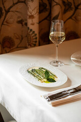 Grilled asparagus spears served with olive oil basil leaves and glass of white wine on restaurant table