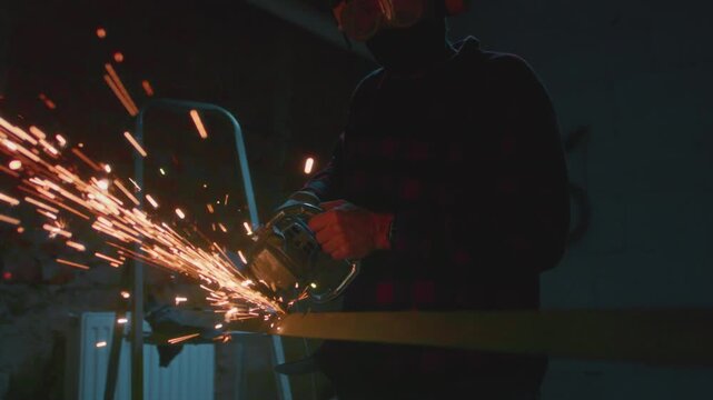 Man working at factory cuts metal with a grinder. Male at a construction site cuts off piece, bright flying sparks and particles of material fly. Guy Industrial worker use angle grinder cutting metal