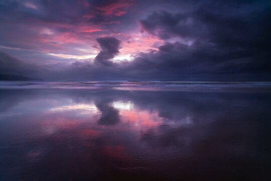 Dramatic winter sky at sunset reflected on a beach with wet sand at low tide, North Devon, England, UK