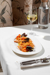 Pasta with mussels shrimp and rich tomato sauce served on white plate with glass of white wine