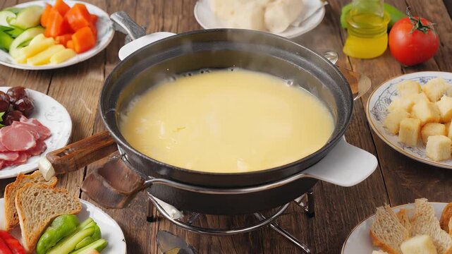 Fondue Party: Melting Cheese with Bread, Meat, and Vegetables in a Traditional Ceramic Pot on a Wooden Table.