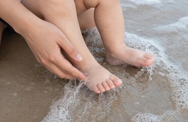 Gentle maternal hand touches tiny baby feet immersed in soft ocean surf and wet sand during a relaxing summer beach vacation