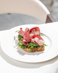 Toast topped with sliced cured beef fresh greens and grated cheese served on elegant white plate