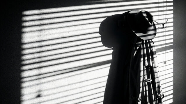 Film noir silhouette of coat and hat with window blind shadows
