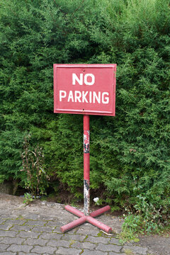 NO PARKING sign on red background in front of green bushes