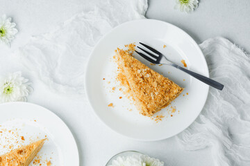 Layered puff pastry dessert cake with cream filling and crumbs on plate with fork and white flowers