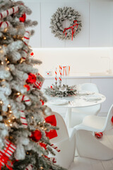 Decorated christmas tree with red bows and lights in a white room with a festive table setting.