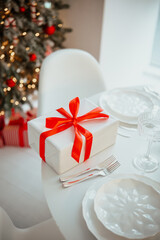 White gift box with red ribbon on table, festive holiday celebration, decorated Christmas tree background