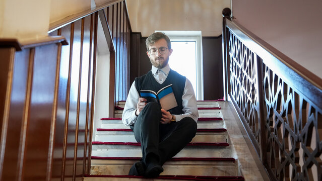 Young Muslim man reading an Islamic religious book on mosque stairs. Concept of worship and spiritual seeking in Ramadan. Muslim student studying theology at masjid. Religious education,