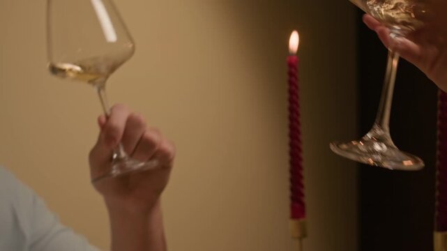 Handheld shot of young man and woman holding hands together, drinking white wine while dining at festive table during home celebration